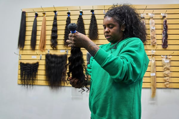 Sholanda Addison, a hair stylist who specializes in human hair extensions, inspects a bundle of curly hair while shopping at Starhair Factory in Doraville, Ga., Monday, May 5, 2025. (AP Photo/Stephanie Scarbrough)
