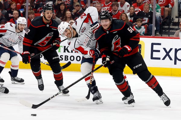 Carolina Hurricanes' Eric Robinson (50) battles for the puck with Washington Capitals' Nic Dowd (26) with Hurricanes' Jesperi Kotkaniemi (82) nearby during the first period of Game 4 of a second-round NHL hockey playoff series in Raleigh, N.C., Monday, May 12, 2025. (AP Photo/Karl DeBlaker)