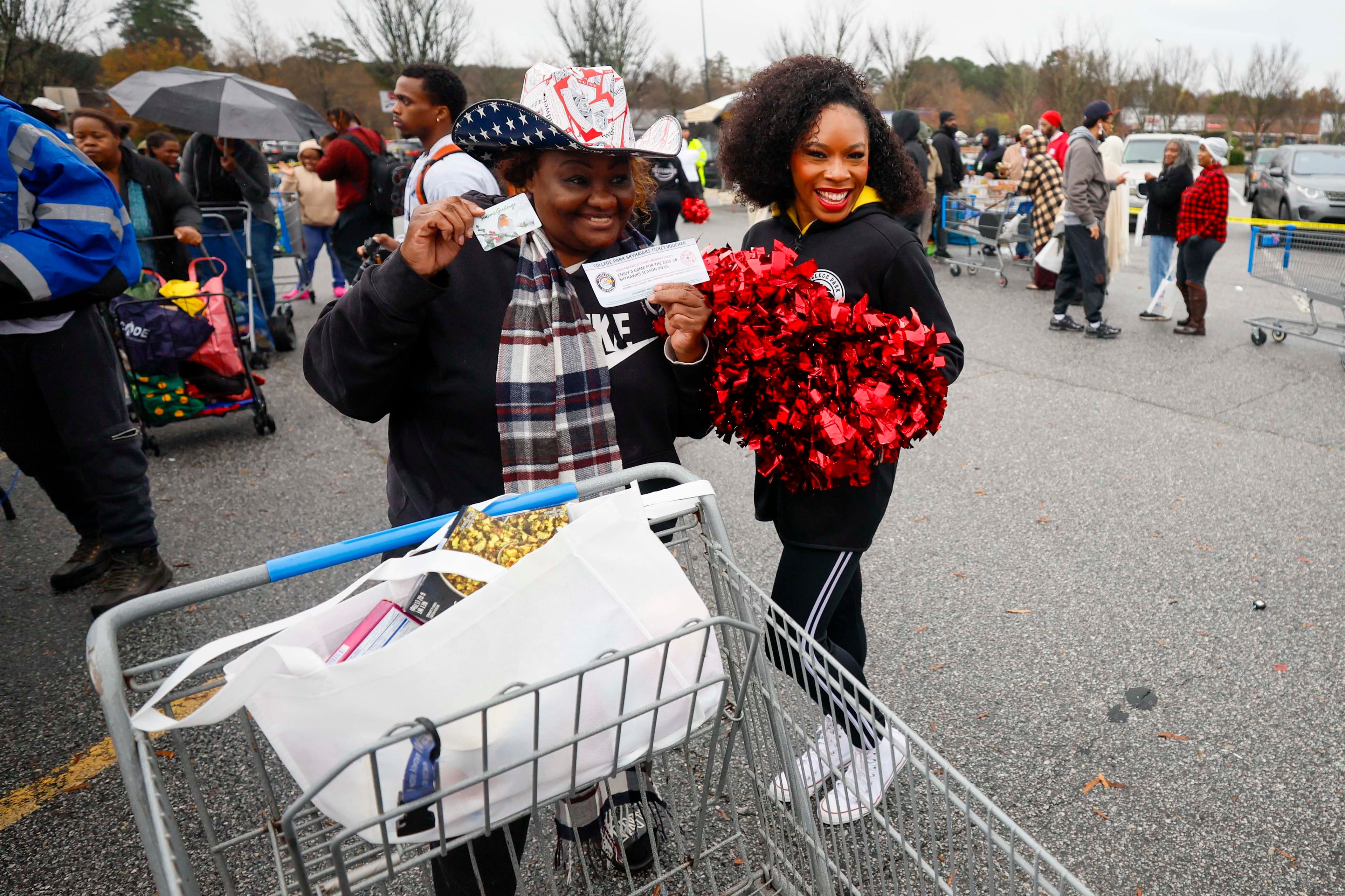 Pamela Brown from Atlanta poses with her Skyhawks ticket voucher and gift card alongside a Skyhawks cheerleader at the “Greens and Things" Thanksgiving giveaway on Tuesday, Nov. 24, 2025. (Miguel Martinez/AJC)