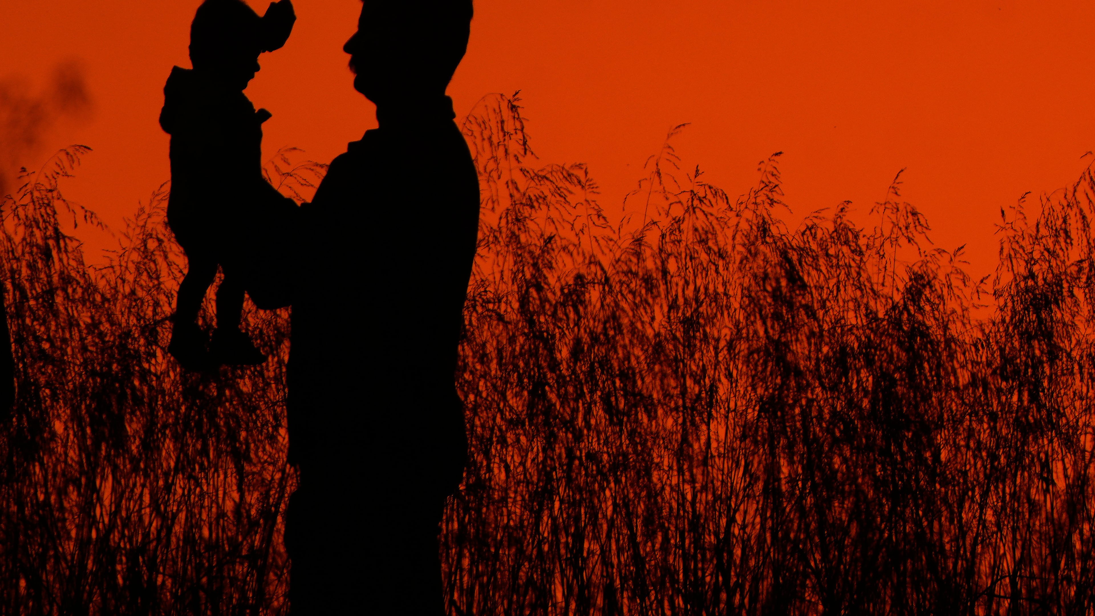 A man holds up a child while walking in a park at sunset, Wednesday, Oct. 15, 2025, in Shawnee, Kan. (AP Photo/Charlie Riedel)