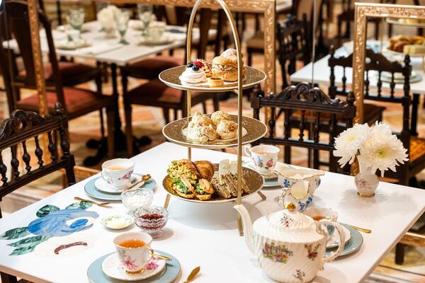A three-tiered tea stand filled with snacks sits on a table with fine china tea service and flowers in a small vase.