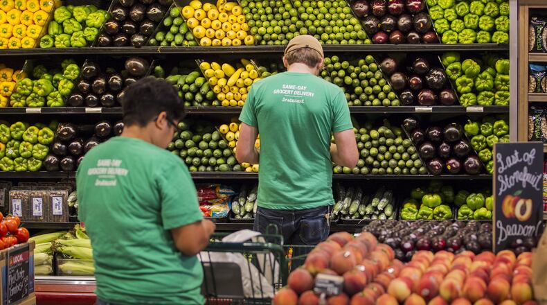 In this file photo, Instacart shoppers Jayme Romero, left and Adam Alfter check their iPhones to get the list of what customers want from a Whole Foods grocery store.