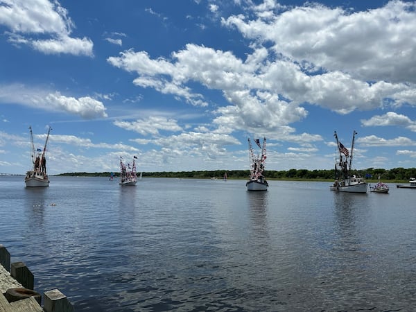 Several shrimp boats spread out in a row on the water, taken from a distance