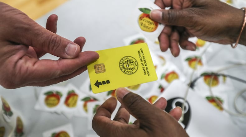 In this 2018 file photo, poll worker Carlos Bennett at Henry W. Grady High School in Atlanta hands out voting stickers as he collects electronic ballot cards. JOHN SPINK/JSPINK@AJC.COM