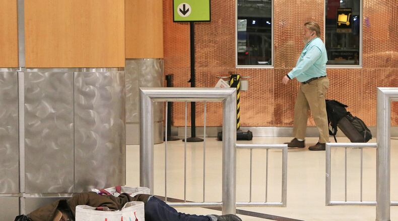 A man (left) sleeps on the ground in the domestic terminal of Hartsfield-Jackson International Airport as flight passengers (right) walk toward security on Friday, February 7, 2020, in Atlanta. Many of Atlanta’s homeless sleep overnight in the airport’s domestic terminal when the city experiences frigid winter temperatures. The man (left) wished not to be identified. (Christina Matacotta/crmatacotta@gmail.com)