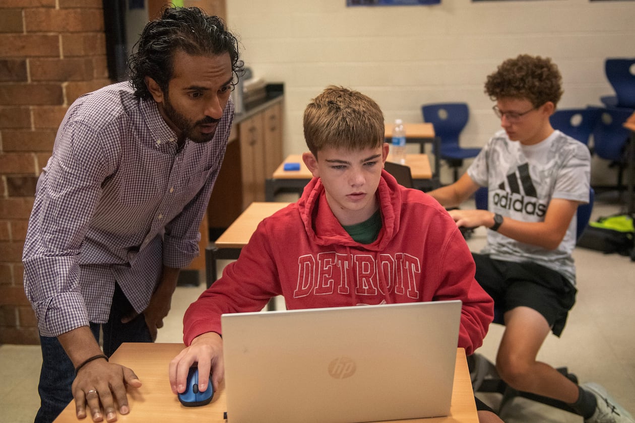 From left, Raghu Arghal teaches students Nathan Wright and Graham Long about the ethics of artificial intelligence as they complete an assignment for an AI summer class at Novi High School. Arghal and fellow teacher Adithya Sairamachandran are leading AI Scholars, an in-person boot camp that exposes high school students to fundamental AI concepts and guides them to build a project with social impact. (Neo Hopkins/The Detroit News)