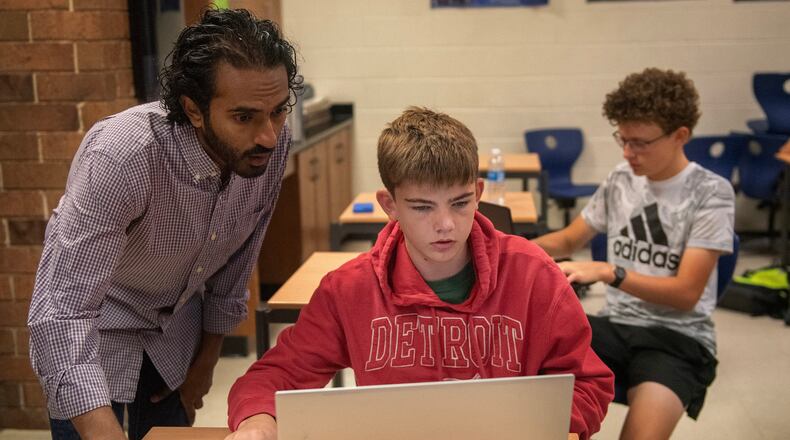 From left, Raghu Arghal teaches students Nathan Wright and Graham Long about the ethics of artificial intelligence as they complete an assignment for an AI summer class at Novi High School. Arghal and fellow teacher Adithya Sairamachandran are leading AI Scholars, an in-person boot camp that exposes high school students to fundamental AI concepts and guides them to build a project with social impact. (Neo Hopkins/The Detroit News)