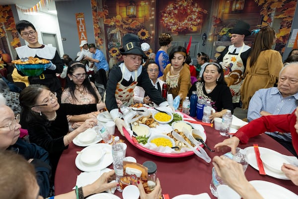 A server wearing a pilgrim costume serves a large platter of food to a table during the Thanksgiving Celebration at the First Senior Center, on Thursday, Nov. 20, 2025, in Norcross, Ga. (Jason Getz / AJC)