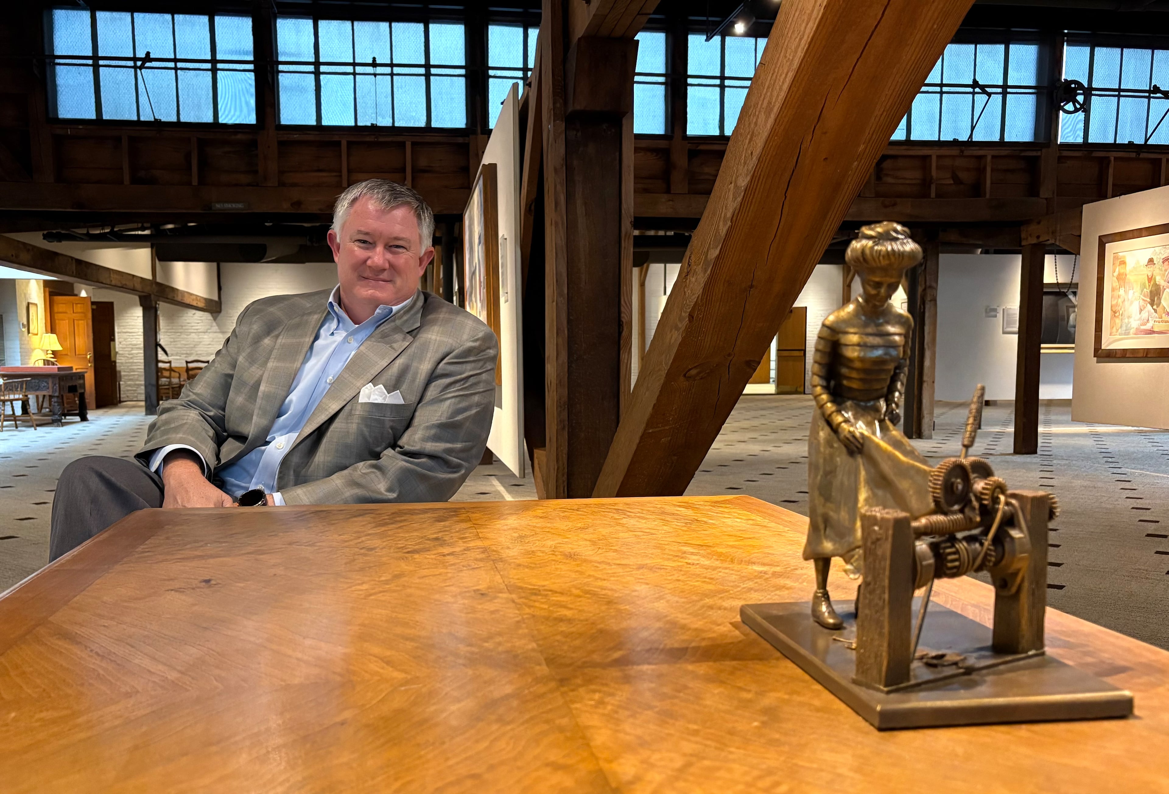 Pace Halter, president of W.C. Bradley Co. Real Estate, posed for a photo on Sept. 3, 2025, next to a small statue representing the origin story of Synovus, which involved a mill worker getting her dress stuck in a loom in 1888. (Zachary Hansen/AJC)