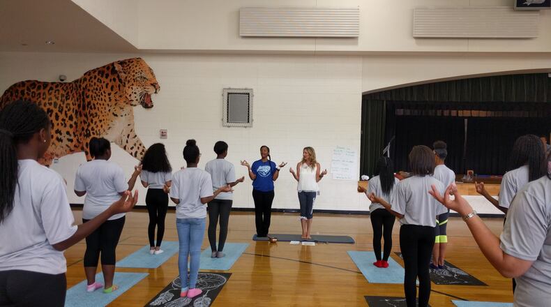 May 18, Atlanta: Cheryl Crawford ( center right), of Grounded Kids Yoga, leads Sandtown Middle School students in yoga with P.E. teacher Tracy Baker (next to her in blue shirt), a former science teacher who will be teaching yoga full-time at the school in the fall after earning her yoga teaching credential from Crawford. This session at the Fulton County school's gym was a practice run.
