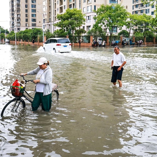In this photo released by Xinhua News Agency, residents try to get through a flooded road in the aftermath of Typhoon Bavi in Yueqing City, eastern China's Zhejiang Province, July 12, 2026. (Jiang Han/Xinhua via AP)