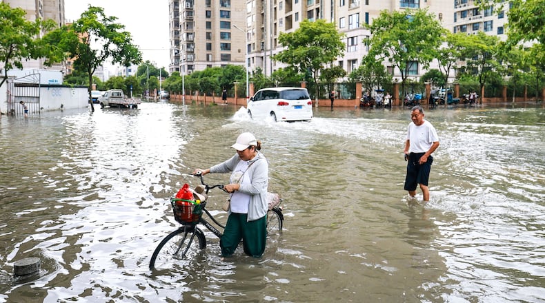 In this photo released by Xinhua News Agency, residents try to get through a flooded road in the aftermath of Typhoon Bavi in Yueqing City, eastern China's Zhejiang Province, July 12, 2026. (Jiang Han/Xinhua via AP)