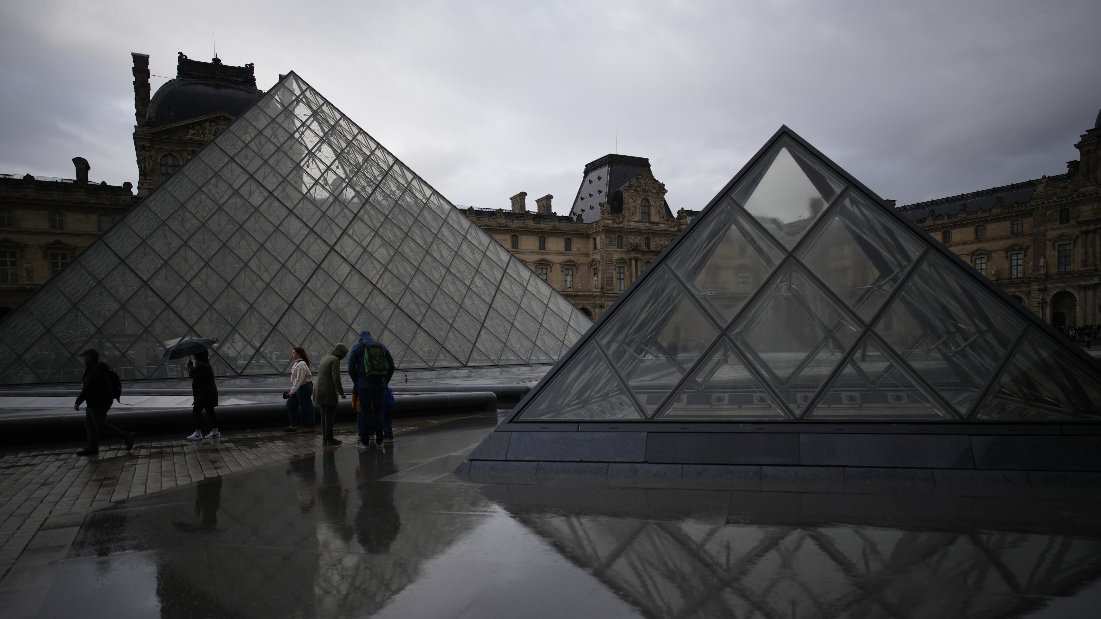 People tour the courtyard of Le Louvre museum in the rain Monday, Oct. 27, 2025 in Paris. (AP Photo/Christophe Ena)