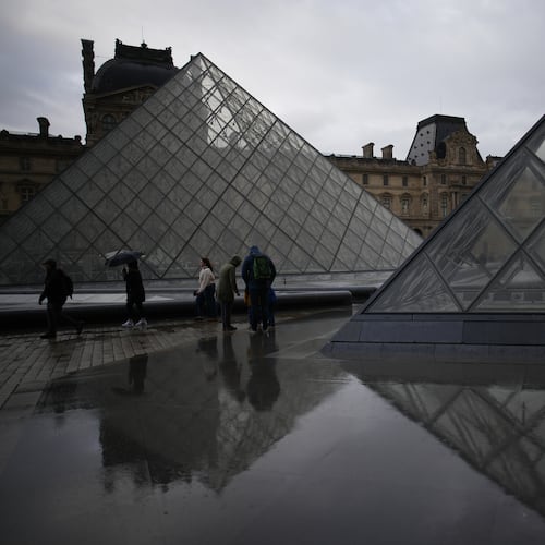 People tour the courtyard of Le Louvre museum in the rain Monday, Oct. 27, 2025 in Paris. (AP Photo/Christophe Ena)
