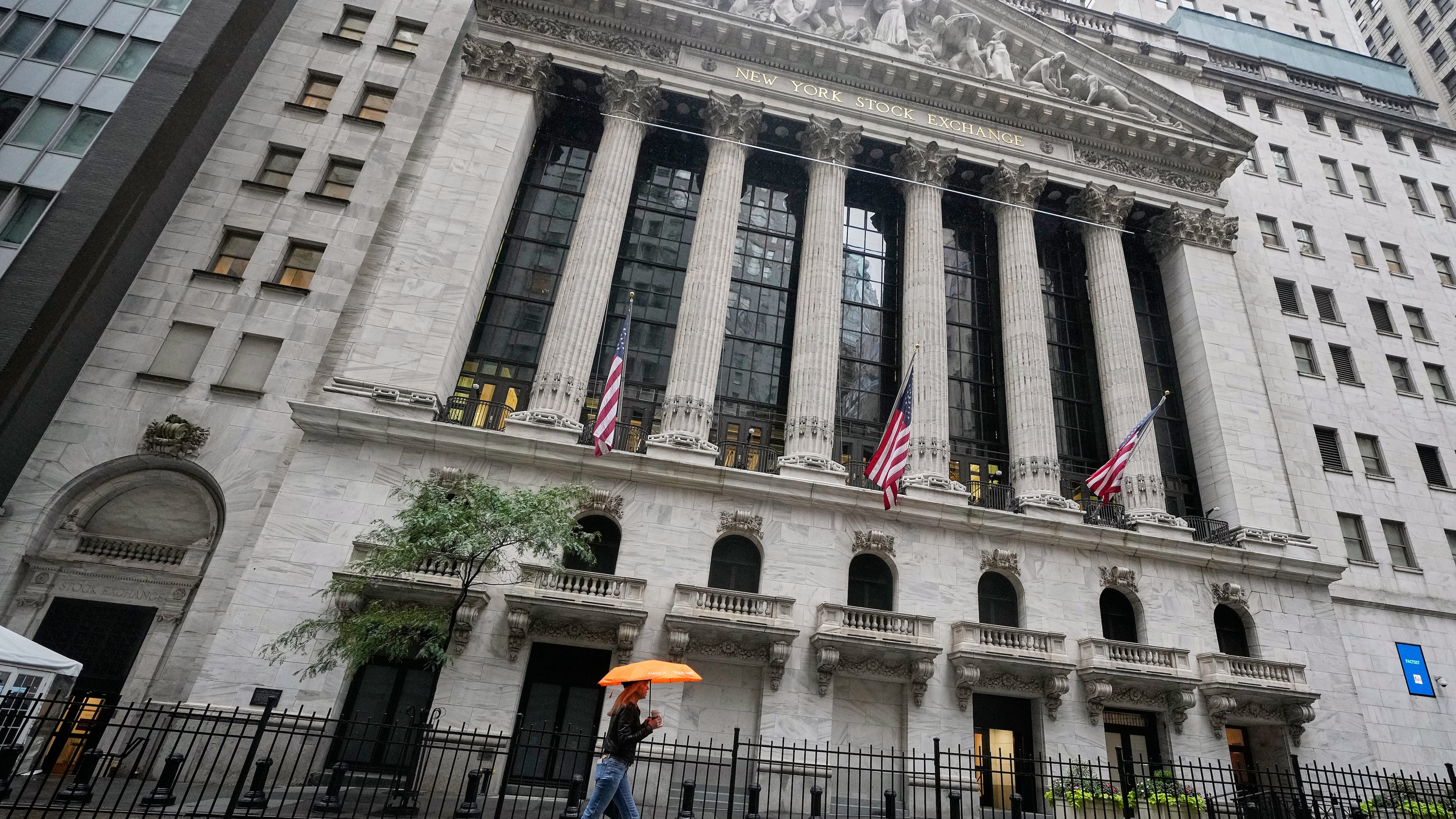 A woman with an umbrella passes the New York Stock Exchange, Monday, Oct. 13, 2025. (AP Photo/Richard Drew)