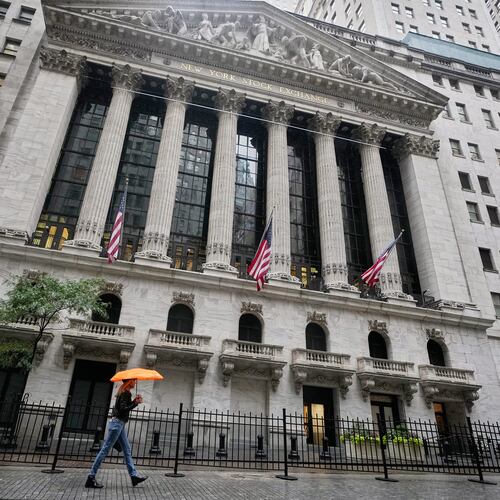 A woman with an umbrella passes the New York Stock Exchange, Monday, Oct. 13, 2025. (AP Photo/Richard Drew)