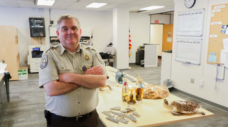 Chris Andrews poses for a photo with confiscated goods, June 4, 2026, at his office in the Ted Stevens Anchorage International Airport in Anchorage, Ala. (James Daggett/Alaska Public Media via AP)