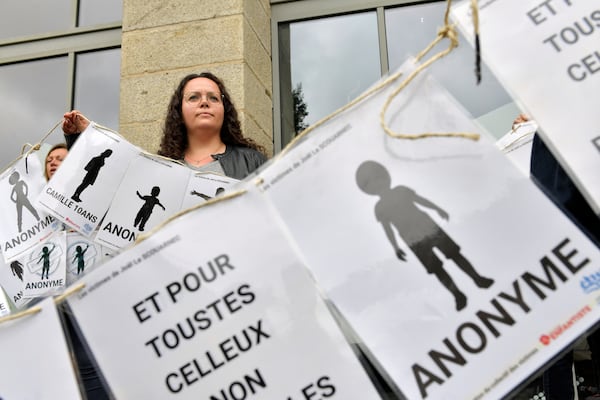 A woman peers behind a banner representing anonymous victims during a demonstration ahead of the verdict in the trial of Joel Le Scouarnec, a 74-year-old former surgeon, accused of raping and sexually assaulting 299 children, Wednesday, May 28, 2025 in Vannes, Brittany, western France. (AP Photo/Mathieu Pattier)