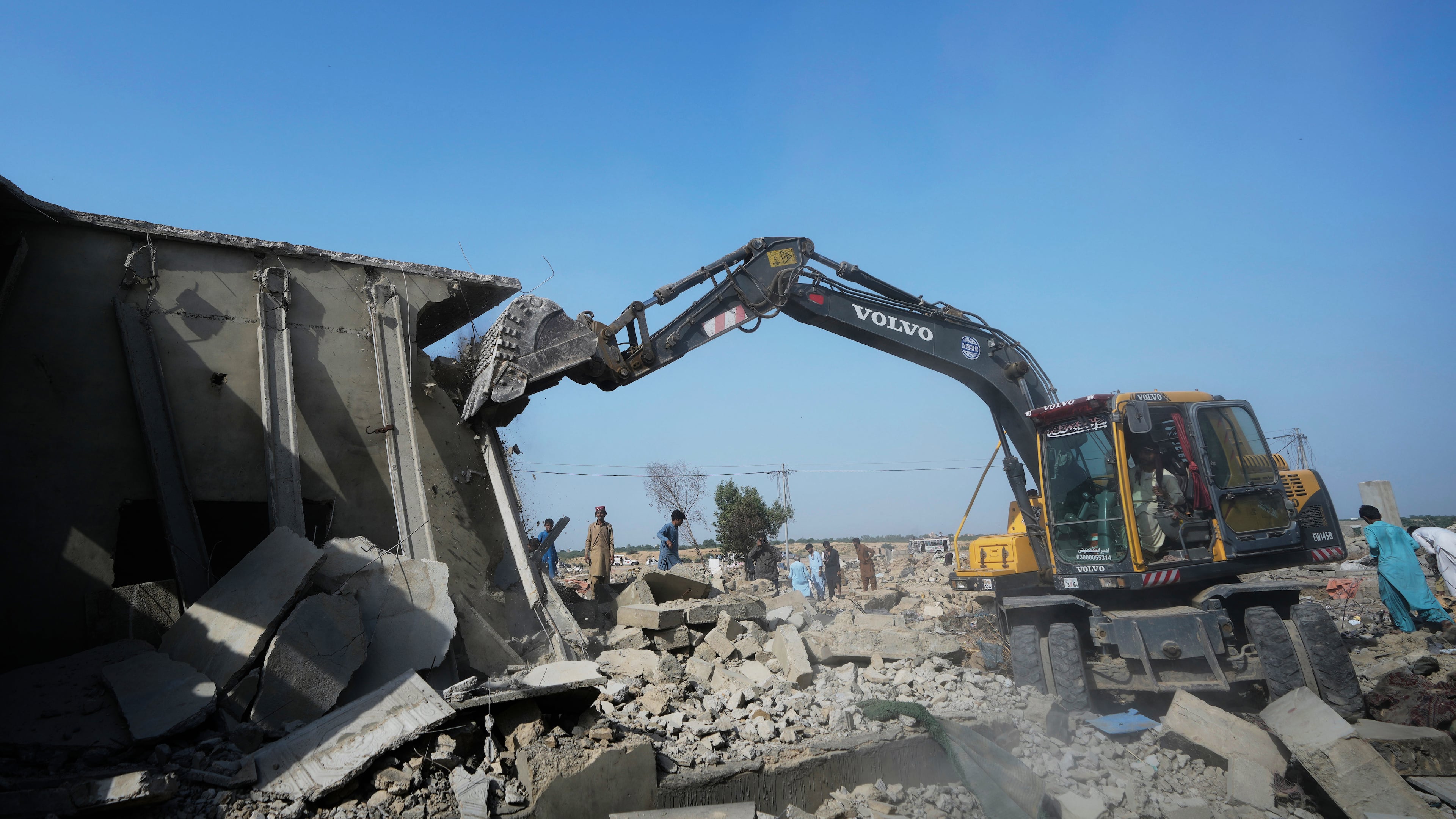 A hydraulic shovel demolish a structure during an operation against illegal settlement of Afghan refugees conducted by local government, on the outskirts of Karachi, Pakistan, Wednesday, Oct. 15, 2025. (AP Photo/Fareed Khan)