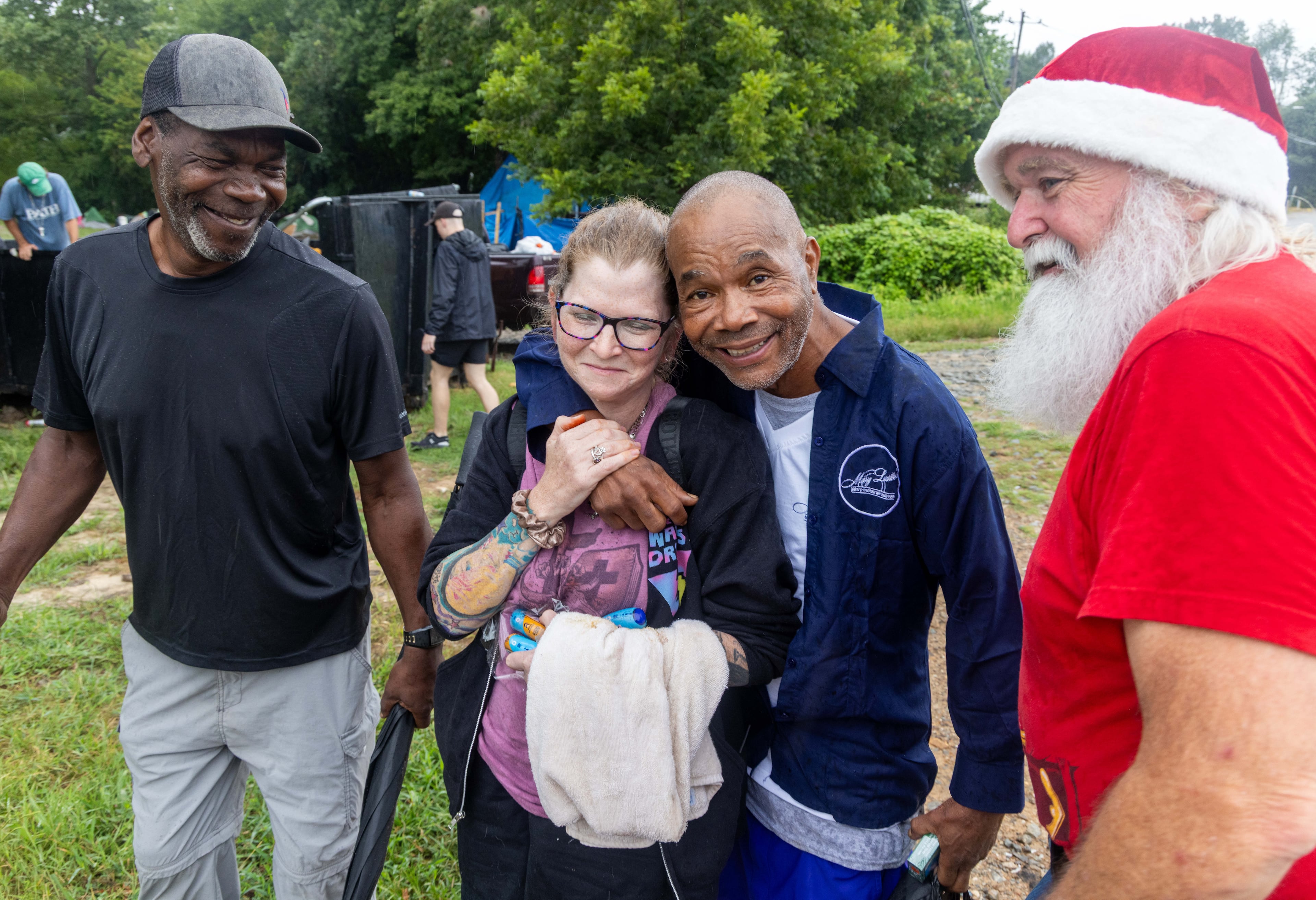 Santa for the Homeless volunteer Danielle Jones-Tetteh (second from left) gets a hug of gratitude from Donald as she and Randy Smith (far right) help set up tents with food, clothing and other needs near a homeless encampment in Gainesville. (Phil Skinner for the AJC)