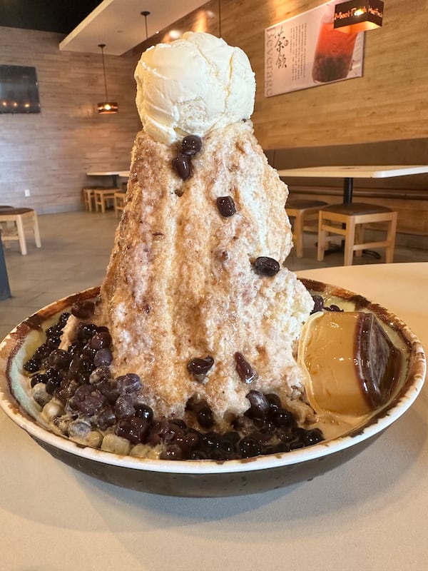 A towering plate of shaved ice topped with a scoop of ice cream and sprinkled bits of dark boba.
