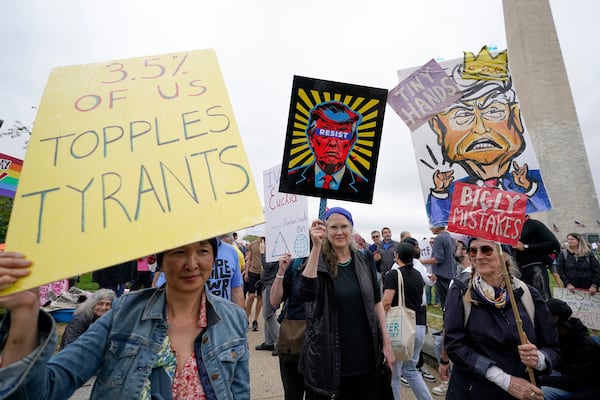 Demonstrators hold up signs during a "Hands Off!" protest against President Donald Trump at the Washington Monument in Washington, Saturday, April 5, 2025. (AP Photo/Jose Luis Magana)