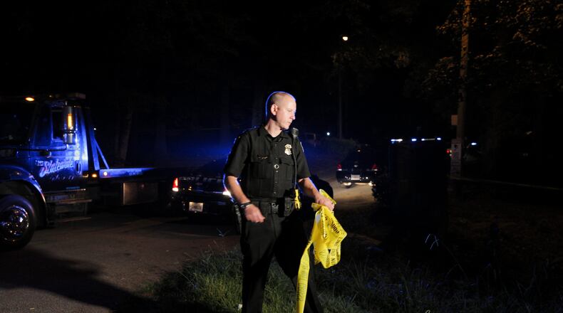 A DeKalb County police officer replaces police line tape at the entrance of a condominium community near Decatur on Friday morning after a man was shot during a robbery.