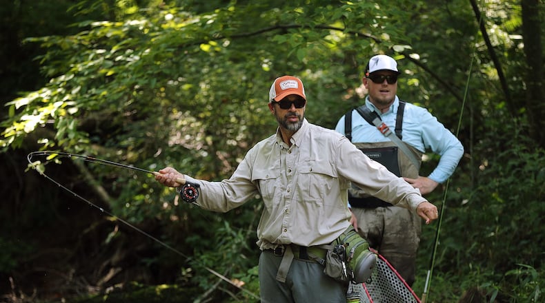 Atlanta resident Louis Cahill (left), 55, hooks a trophy-size trout while Justin Pickett, 33, of Newnan, spots them on a catch and release stream at Noontootla Creek Farms. Curtis Compton/ccompton@ajc.com