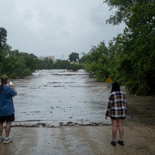 Mike Erulenfeld and Kala Martin watch as the Pedernales River floods near Old Kerr Highway on Thursday, July 16, 2026, in Fredericksburg, Texas. (AP Photo/Joel Angel Juarez)