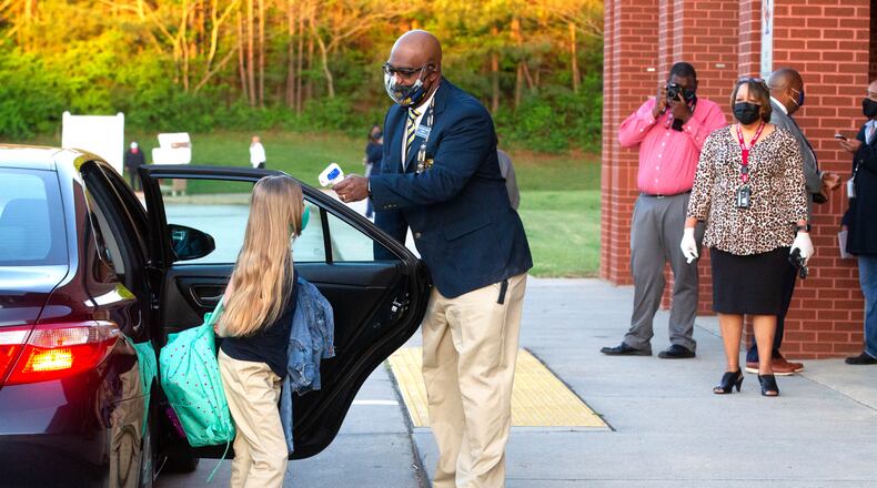 Jackson Elementary School principal William Greene takes the temperature of a student as she returns to school for in-person learning on Monday. After remaining all-remote for most of the academic year because of COVID-19 concerns, Clayton brought pre-kindergarten to fifth-graders back to school this week for the first time. STEVE SCHAEFER FOR THE ATLANTA JOURNAL-CONSTITUTION