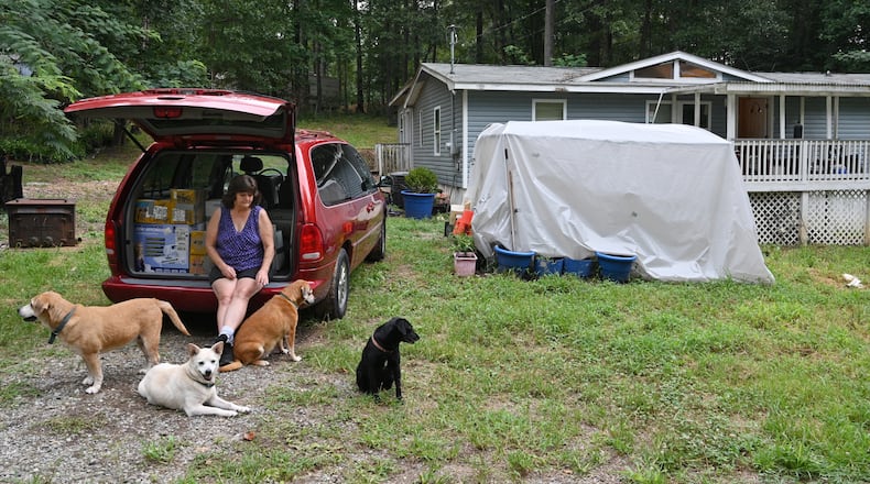 Kathy Poland-Jones plays with her dogs as she sits on the back of her van where she has loaded up boxes for moving out at their home in Canton on Tuesday. Poland-Jones, 65, had lost her full-time job and took part-time work, but she hasn’t been able to keep up her payments. She got an eviction notice in June. “Nobody would rent to me before,” she said. “I have no idea where to go.” (Hyosub Shin / Hyosub.Shin@ajc.com)