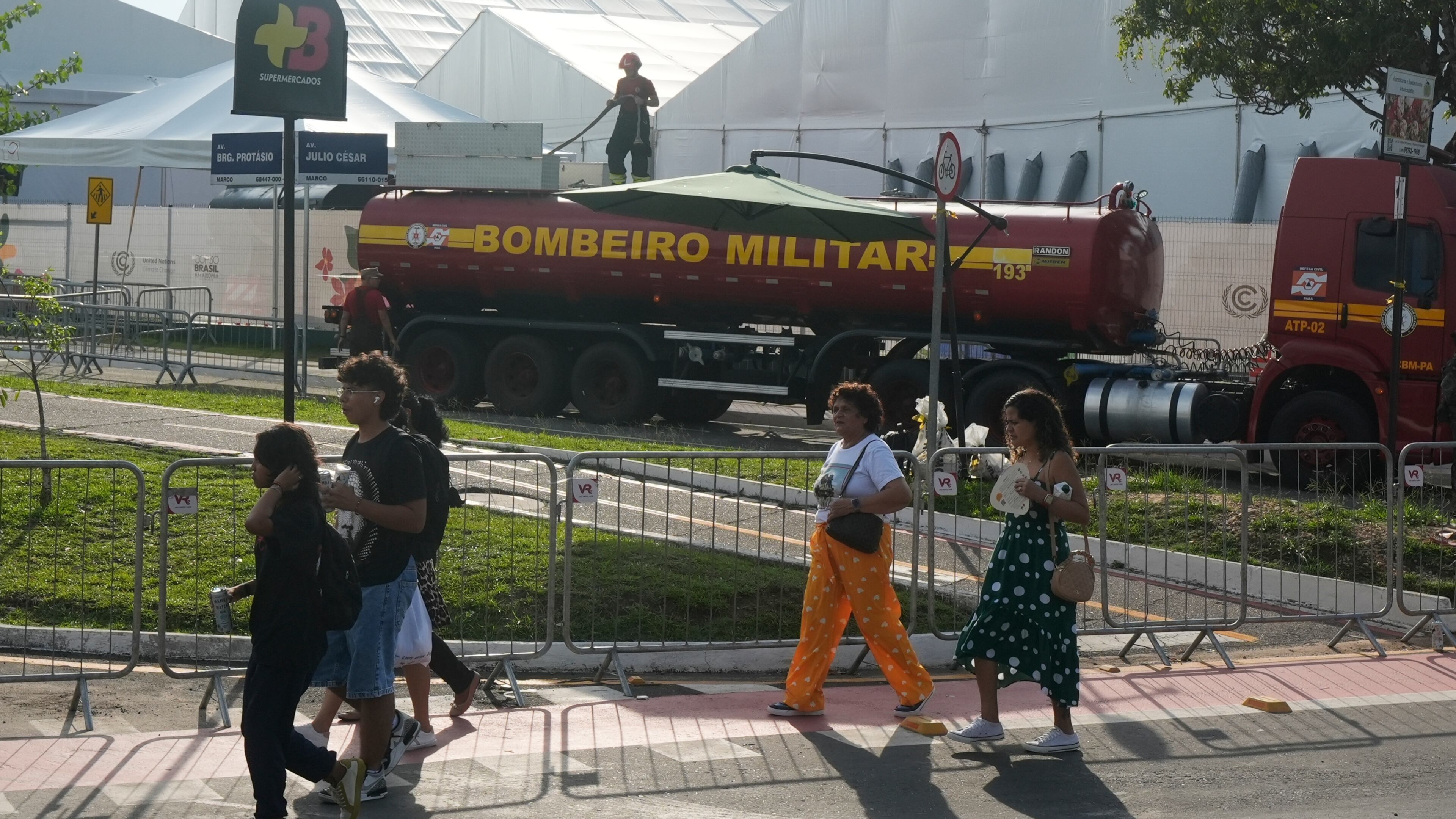 People walk past as a firefighter works at the COP30 U.N. Climate Summit following a fire, Thursday, Nov. 20, 2025, in Belem, Brazil. (AP Photo/Fernando Llano)