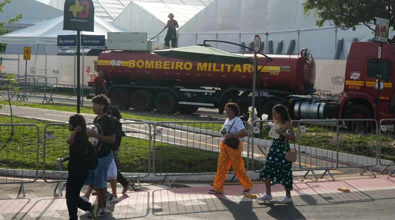 People walk past as a firefighter works at the COP30 U.N. Climate Summit following a fire, Thursday, Nov. 20, 2025, in Belem, Brazil. (AP Photo/Fernando Llano)