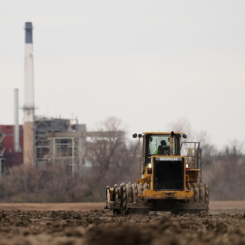 A worker prepares a plot of land for an AI data center, with a retired power plant being refurbished to provide electricity for the facility in the distance, March 24, 2026, in Independence, Mo. (Charlie Riedel/AP)