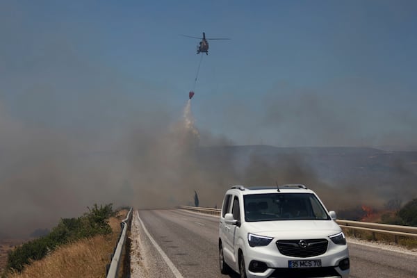 A helicopter drops water to extinguish a fire in Cesme, near Izmir, Turkey, Thursday, July 3, 2025. (Cengiz Malgir/Dia Photo via AP)