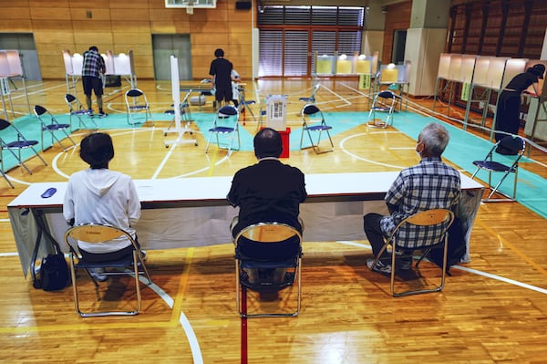Voters, back, fill in their ballots for the upper house election at a polling station as representatives of a local election administration commission observe at a polling station Sunday, July 20, 2025, in Tokyo. (AP Photo/Eugene Hoshiko)