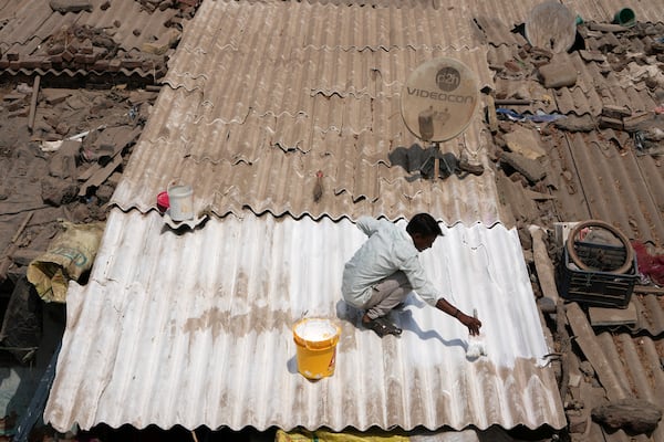 A man applies reflective paint to the roof of a house that helps keep the indoors cooler in Ahmedabad, India, Wednesday, April 2, 2025. (AP Photo/Ajit Solanki)