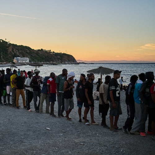 Migrants who crossed from Morocco into Spain line up for food distribution on a beach in the Spanish enclave of Ceuta, Monday, Aug. 3, 2026. (AP Photo/Bernat Armangue)