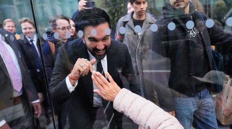 New York City mayoral candidate Zohran Mamdani waves to Rita Bellevue as she waits at a bus stop in New York, Monday, Oct. 27, 2025. (AP Photo/Seth Wenig)