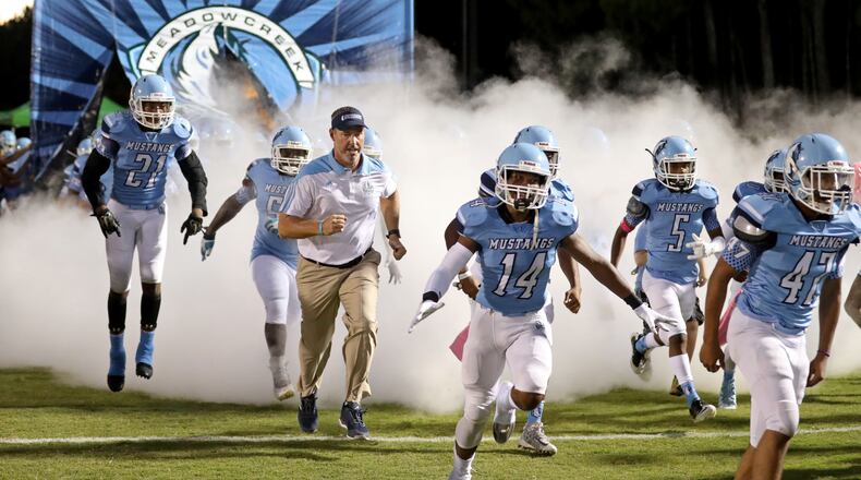 Meadowcreek head coach Jason Carrera runs onto the field with players before a game.