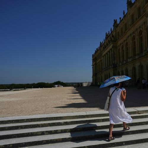 A woman shields herself from the sun with an umbrella as she walks in the garden of the Palace of Versailles, outside Paris, Monday, June 22, 2026. (AP Photo/Thibault Camus)