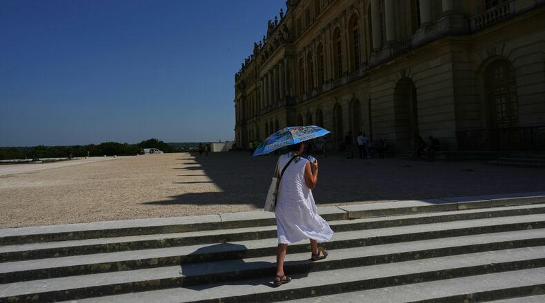 A woman shields herself from the sun with an umbrella as she walks in the garden of the Palace of Versailles, outside Paris, Monday, June 22, 2026. (AP Photo/Thibault Camus)