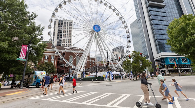 People cross Centennial Olympic Park Drive in front of the SkyView Atlanta Observation Wheel, a 20-story Ferris wheel with gondolas on Saturday, July 15, 2023. The SkyView Wheel is celebrating its 10th anniversary in downtown Atlanta. (Steve Schaefer/steve.schaefer@ajc.com)