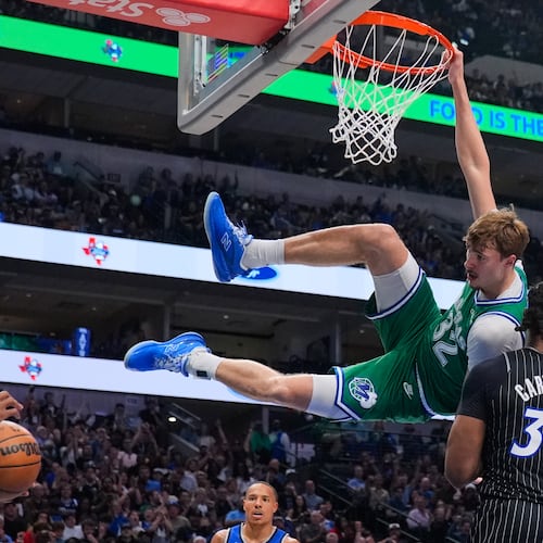 Dallas Mavericks forward Cooper Flagg (32) hangs on the rim after dunking over Orlando Magic's Wendell Carter Jr. (34) and Jevon Carter, left, in the first half of an NBA basketball game Friday, April 3, 2026, in Dallas. (AP Photo/Tony Gutierrez)