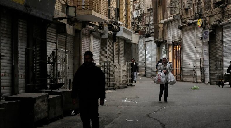 A woman carries her groceries as people walk along the mostly empty Tehran traditional main bazaar, where most shops are closed, in Tehran, Iran, Tuesday, March 10, 2026. (AP Photo/Vahid Salemi)