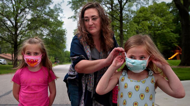 Jenny Berla helps her twins Isla, left, and Elodie with their masks as they approach their sister's school to pick her up after class on Wednesday, May 19, 2021. Berla, who is planning to send the girls to kindergarten this fall, is concerned that dropping mask mandates before young children are eligible for vaccinations leave them open to risk. (Robert Cohen/St. Louis Post-Dispatch/TNS)