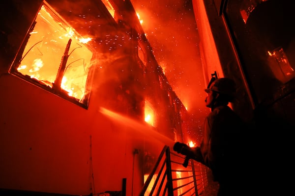 FILE - A firefighter works from a deck as the Palisades Fire burns a beach front property Jan. 8, 2025, in Malibu, Calif. (AP Photo/Etienne Laurent, File)
