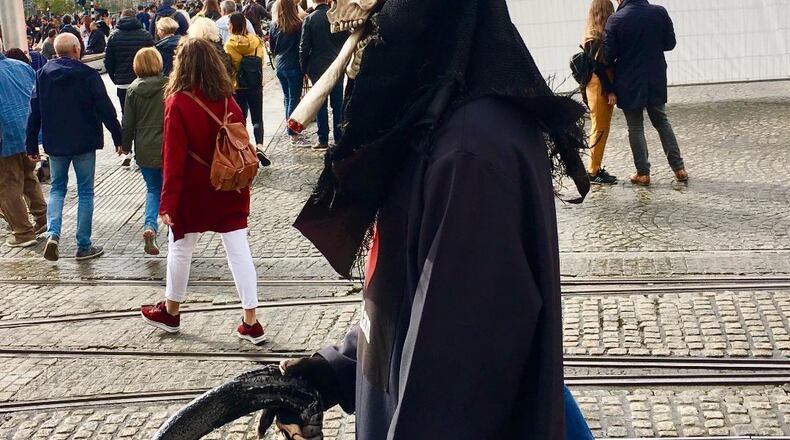 If this fellow approaches your door make sure you follow strict social distancing with a minimum 6 feet separation. Or you can simply shut your door and turn out the lights. 
His mask is likely a replica of Vincent van Gogh's famous early work "Skull of a Skeleton with Burning Cigarette," although since this is a recent photo taken in Amsterdam it's likely that isn't a cigarette at all. Bill Banks for the AJC