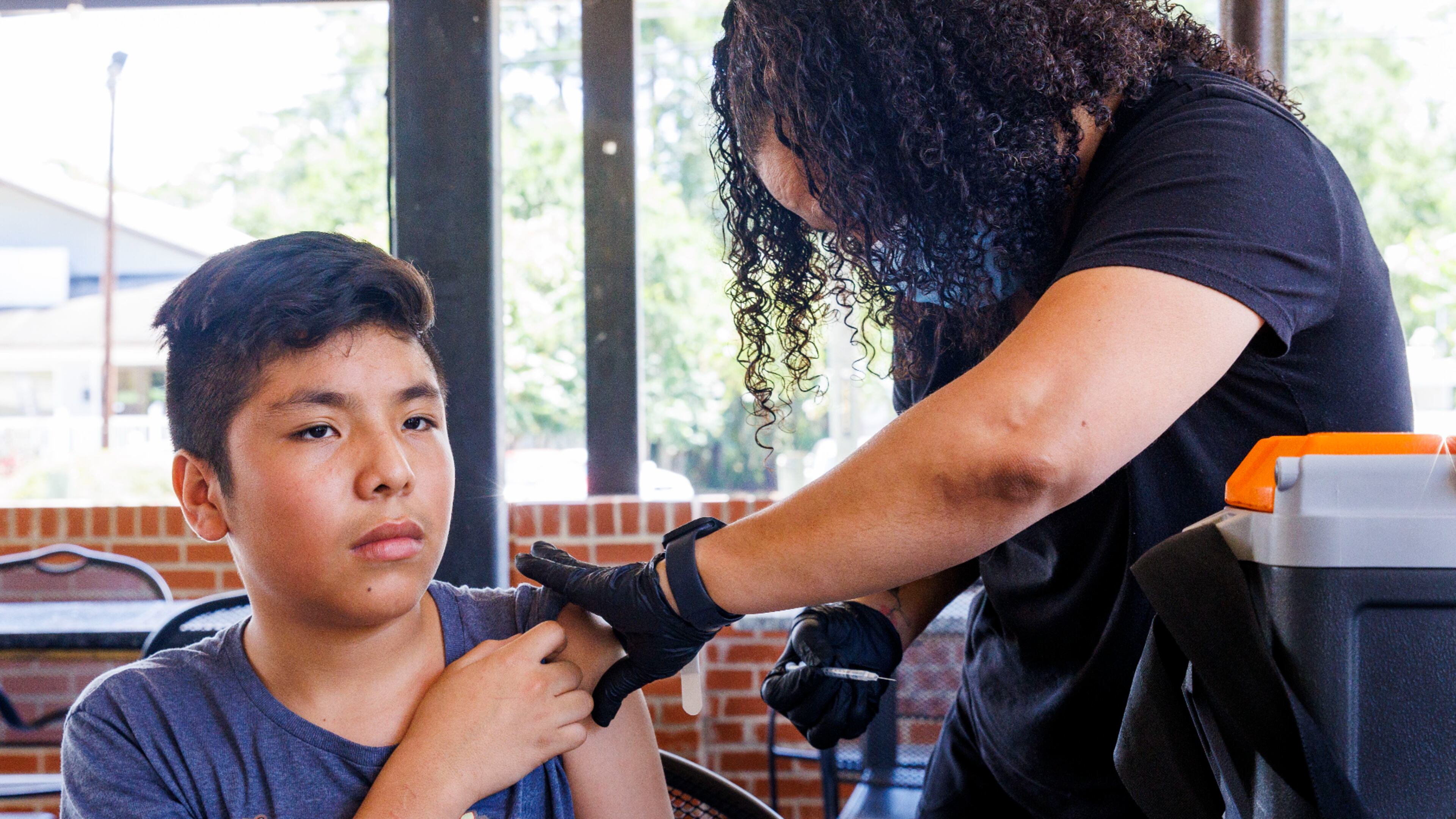 Edson Sebastian Ordonez Guzman (left), 13, awaits his COVID-19 vaccine from Chequella Sharper during a Latino Community Fund Georgia vaccination and community outreach event in Valdosta. The CDC tweaked the vaccine recommendation for healthy children to say it was subject to “shared clinical decision-making” by the parent and doctor. (Colin Hackley for the AJC 2022)