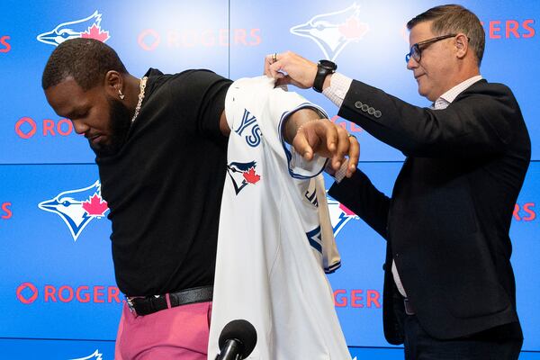 Toronto Blue Jays general manager Ross Atkins, right, puts a Jays jersey on first baseman Vladimir Guerrero Jr. following the signing of Geurrero's 14 year, $500 million dollar contract extension in Toronto on Monday April 14, 2025. (Jon Blacker/The Canadian Press via AP)